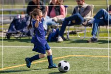 Young girl cheering with her arms in the air as she plays football with parents watching