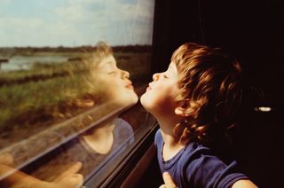 Child pulling faces in the glass window as he travels on a train