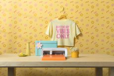 The Cricut Joy Xtra cutting machine on a crafter's desk and a bright yellow wall