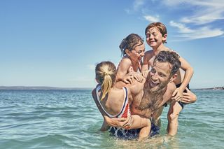 Father holding his three children as they play in the sea on holiday