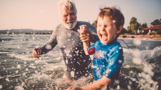 Photo of a little boy and his grandfather spending summer afternoon bathing and swimming in a sea water