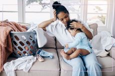 mum holding baby on sofa trying to do washing