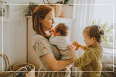 Mother holding young baby whole older child fixes baby's clothing