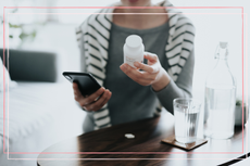 Women holding pill bottle in one hand and smartphone in the other