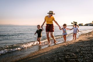 Mother holding hands with three young children on the beach on holiday